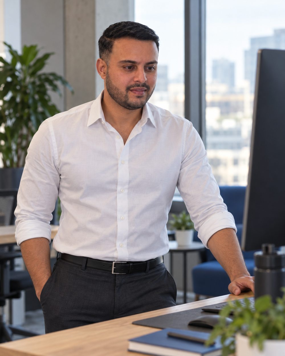 Dil Phagura standing at a desk in an open office, reviewing work on a monitor.
